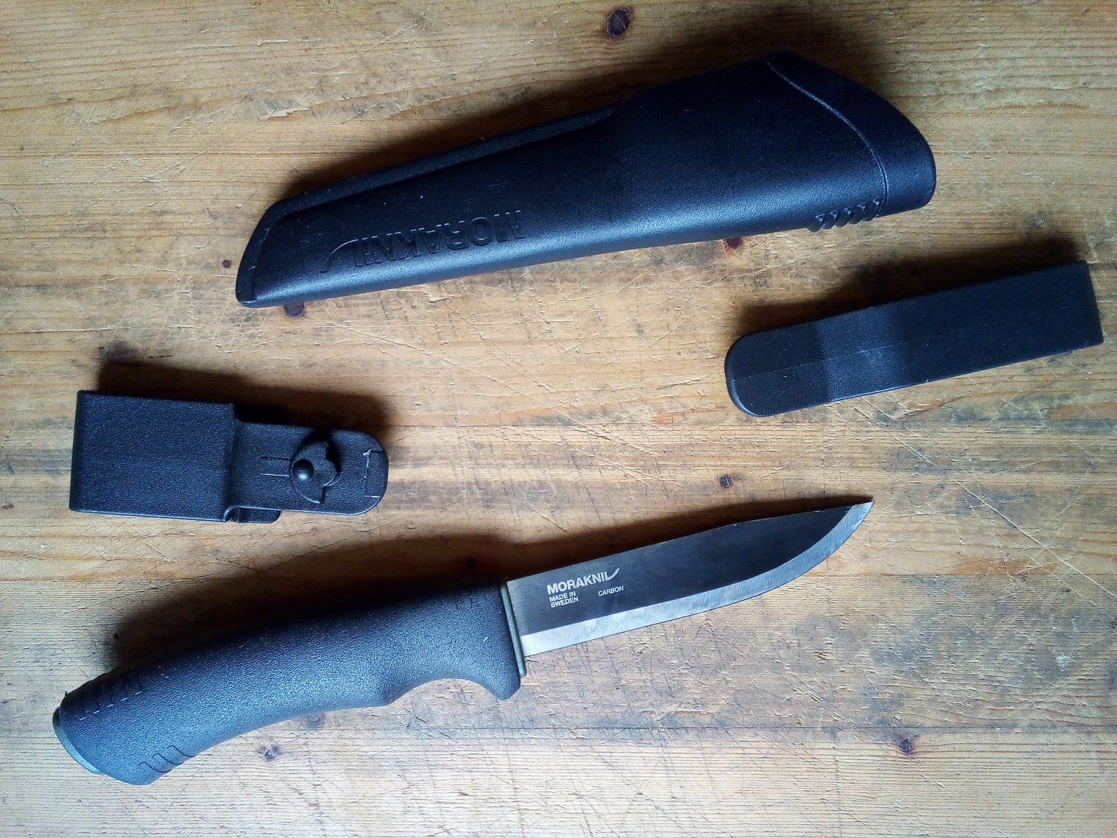 The BUSHCRAFT Black is a 3/4 rat tail tang knife with a total length of 23,2 cm, a blade length of 10,9 cm, with black DLC coating, Scandinavian grind and blade thickness of 3,2mm, weighing 212 grams. The blade is made of carbon steel (C100, 59-60 HRC), while the grip material is rubberised plastic (the sheath material is plastic, as well, and comes with two different belt clips)